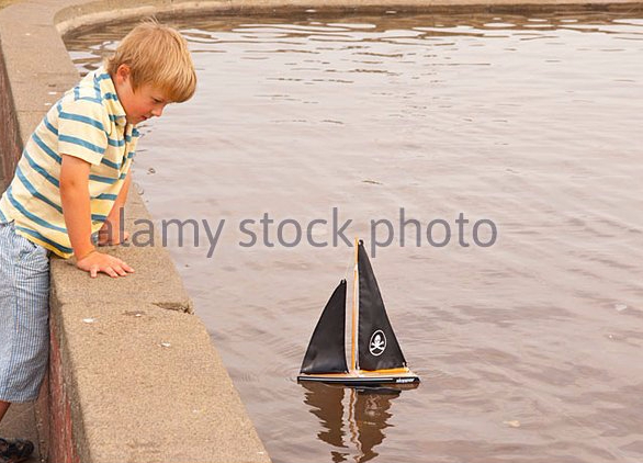 a-small-boy-model-released-sailing-his-toy-boat-at-the-boating-lake-be840t.jpg
